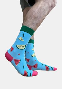 Calcetines azules con puños verdes y acentos rosas, que presentan un patrón de sandía con rodajas y hojas en todo su diseño.