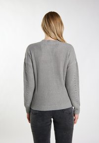 Szary sweter o teksturowanym wzorze dzianiny, jednolity kolor, ściągacz u dołu i ramiona opadające. Brak dodatkowych wzorów lub elementów metalowych widocznych.