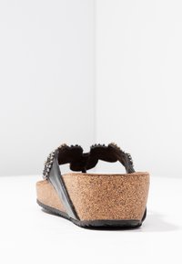 Sandalo con zeppa in pelle nera, suola in sughero, decorazioni in perline sui cinturini e design aperto sul retro. Superficie testurizzata con tacco piatto.