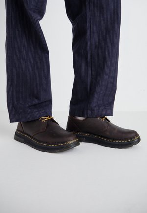 Brązowe skórzane buty z okrągłymi noskami, żółtym przeszyciem i czarnymi gumowymi podeszwami. W zestawie z granatowymi spodniami w paski.