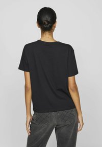 Mustast puuvillasteest, millel on lõdvestatud istuvus, lühikesed varrukad ja ümmargune kaelus, koos tumedate hallide teksadega, millel on tikitud tagataskud.