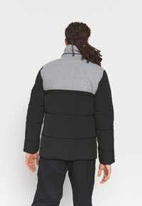 Chaqueta acolchada negra y gris con un alto cuello, que presenta un diseño de panel de contraste, textura acolchada y puños ajustables.