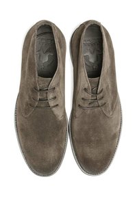 Chaussures en daim marron avec un bout arrondi, trois œillets pour les lacets, semelle plate et finition texturée. L'intérieur présente un logo embossé.