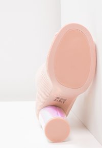 Tacón de punto rosa con una tapa de talón ombré brillante. Suela de goma texturizada con un patrón sutil. Etiquetas visibles en la base del zapato.