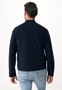 Mörkblå jacka i slätt tyg, med slim fit, ståkrage och ribbade cuffs, bärs över ljusblå denimjeans.