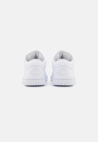 Vita lädersneakers med låg skärning och präglad logotyp på hälen, platt vit sula och slät yta. Minimalistisk design, inga synliga mönster.