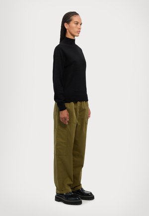 Pull noir à col montant associé à un pantalon cargo ample couleur olive. Des chaussures noires chunky complètent la tenue. Design global minimaliste.