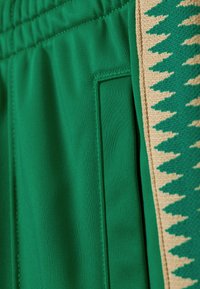 Groene joggingbroek met een textuurstof, elastische tailleband, zijzak en een contrasterend beige zigzagpatroon langs de zijkant.
