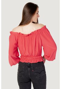 Blusa corallo scollata con vita arricciata ed elasticizzata e maniche lunghe e voluminose. Abbinata a jeans neri a vita alta.