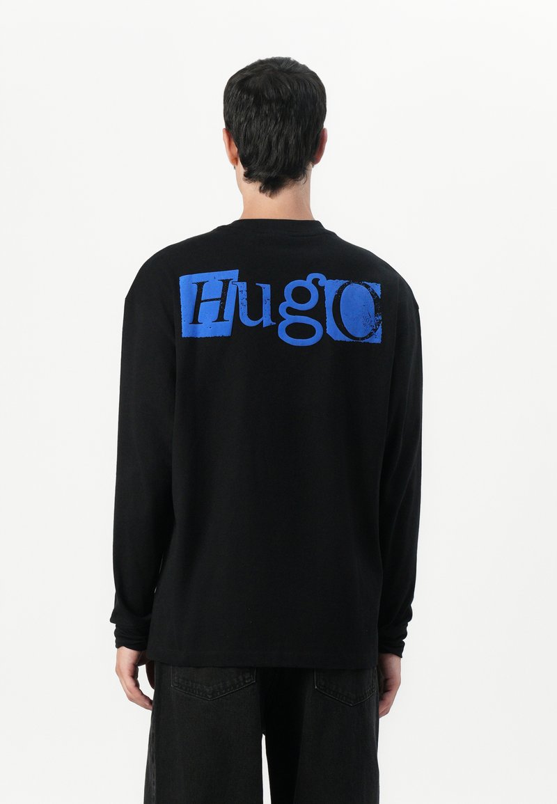 Black long-sleeve shirt with a large blue "Hugo" logo on the back. Cotton material with a relaxed fit and crew neckline.