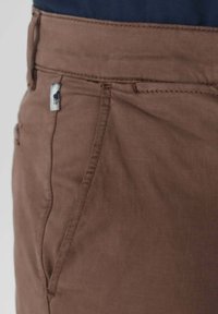 Pantalons en coton marron avec une texture lisse, présentant une poche avant et une petite étiquette logo bleue et blanche à la taille.