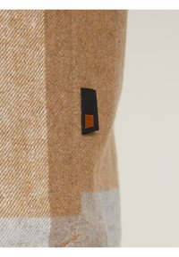 Tejido de mezcla de lana en un patrón de cuadro marrón y gris; presenta una pequeña etiqueta negra con un acento en cuadrado naranja. Textura suave, bordes limpios.