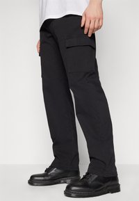 Svarta cargobyxor i bomull, med sidofickor och rak bendesign, tillsammans med svarta snörskor.