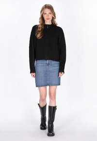 Maglione nero a maglia con un collo alto, abbinato a una gonna di jeans e stivali neri alti fino al ginocchio. Il maglione ha una cerniera frontale.