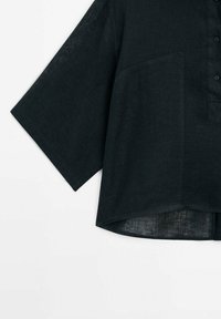 Chemise noire à manches courtes avec larges manches, col boutonné et ourlet légèrement incurvé en tissu léger texturé.