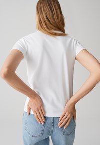 T-shirt bianca a maniche corte con scollo rotondo, abbinata a jeans in denim azzurro chiaro, con una vestibilità aderente e una texture liscia.