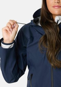 Navy blue waterproof jacket with a high collar, drawstring hood, and a zippered pocket. Fabric features a smooth texture and sleek design.