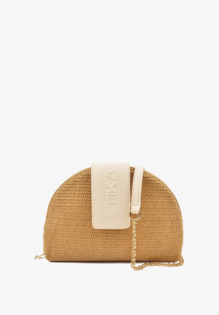 Bolso de paja tejido en tono marrón claro con forma redondeada. Presenta un cierre blanco con el nombre de la marca en relieve y una cadena dorada.