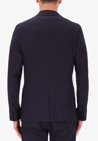 Blazer blu navy in tessuto текстurato, taglio su misura, spacco singolo sul retro e polsini con bottoni. Linee pulite senza ulteriori abbellimenti.