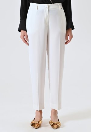 White tailored trousers with a smooth fabric, straight cut, and cropped hem. Paired with gold bow-detail flats for contrast.