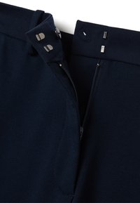 Marineblauwe broeken met een ritssluiting, voorzien van een knoopsluiting en metalen accenten. Glad textuur en schuin geplaatste taillebanddetails.