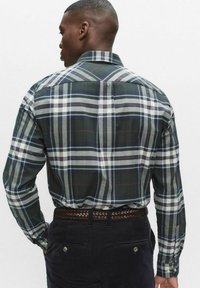 Zielono-szara koszula w kratę z kołnierzykiem na guziki, długimi rękawami i detalem z karczkiem z tyłu, noszona z ciemnymi sztruksowymi spodniami.