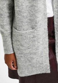 Gray, long cardigan made of soft, textured knit fabric. It features ribbed cuffs and a large front pocket. The hem falls below the waist.