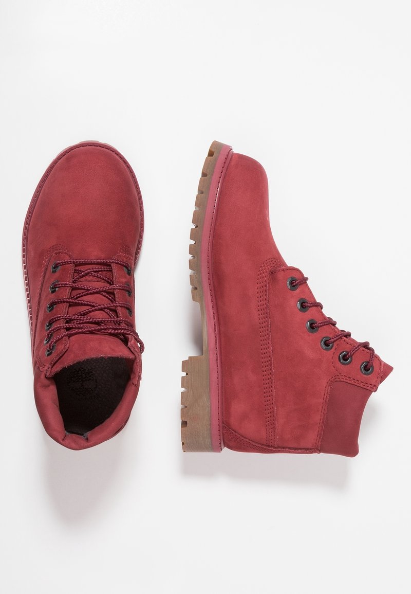 Bottines en daim rouge avec devant lacé, cols matelassés et semelles épaisses en caoutchouc marron, montrées vues de dessus et de côté.