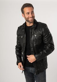 Giubbotto in pelle nera con zip frontale, due tasche sul petto e spalline. Presenta una texture liscia e un taglio classico.