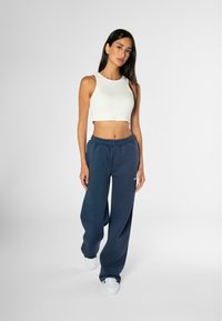 Top corto blanco de canalé y pantalones de chándal de pierna ancha en azul marino con cintura elástica, combinados con zapatillas blancas. Tejido suave, diseño casual.