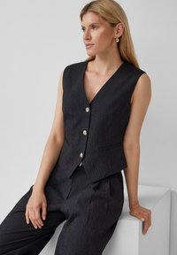 Schwarze Nadelstreifen-Weste mit tiefem V-Ausschnitt, verziert mit goldenen Blumenkknöpfen, taillierte Passform und seitlichen Taschen, kombiniert mit passenden Hosen.