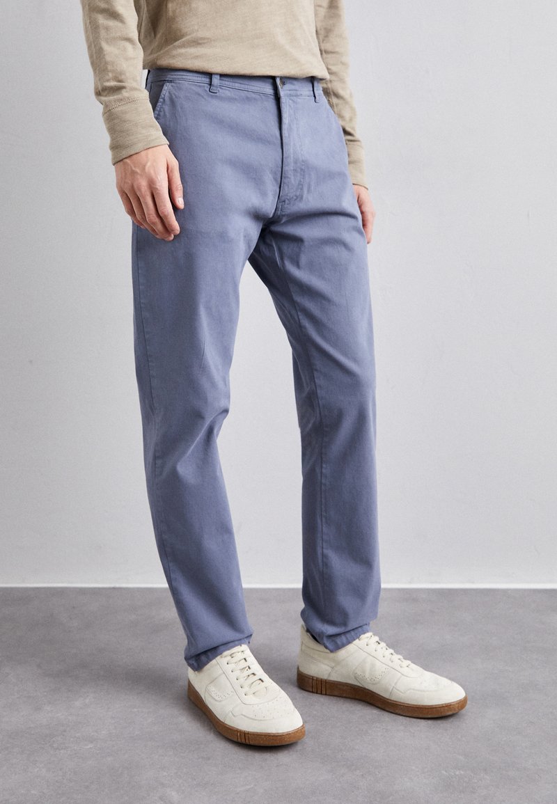 Lysblå bomuldsbukser med flad front og sidelommer, parret med hvide sneakers. Stoffet ser glat ud med en let glans.