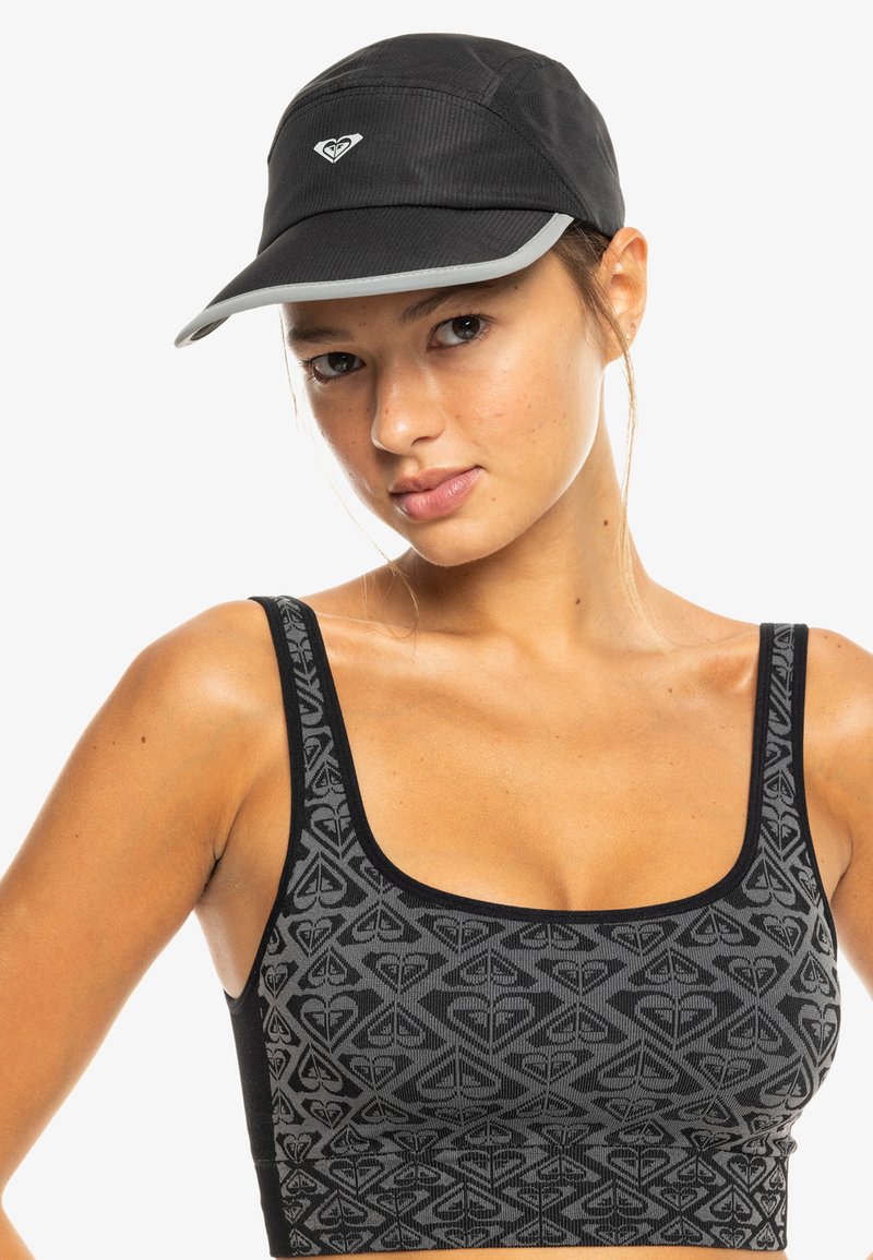 Schwarze Kappe mit grauem Schirm und gesticktem Logo, kombiniert mit einem schwarzen Sport-BH mit geometrischem Muster in verschiedenen Schwarztönen.