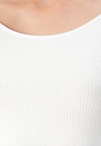 Close-up of a ribbed white sleeveless top worn on bare skin, showing neckline and upper chest area.