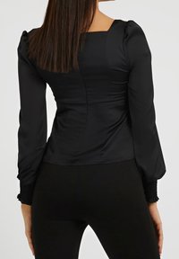 Top nero, aderente, con scollatura quadrata e maniche lunghe. Il materiale è liscio; le maniche presentano polsini arricciati per un effetto texturizzato.