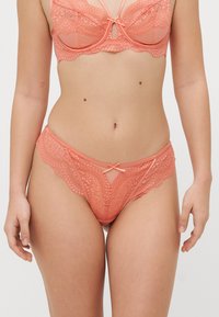 Korallivärinen pitsialusvaatesetti, johon kuuluu bralette, jossa on monimutkaiset aallotetut reunat, sekä yhteensopivat alushousut, joissa on hieno nauha edessä.