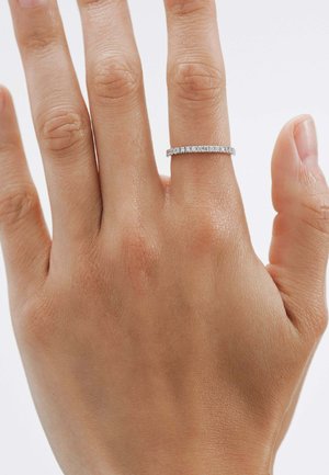 Anillo delgado de plata con pequeñas piedras preciosas estructuradas dispuestas en una línea recta, llevado en una mano con una textura de piel natural.