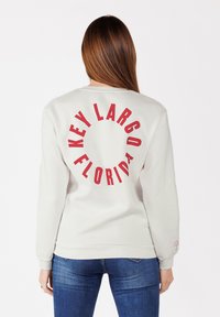 Felpa grigia chiara con "KEY LARGO FLORIDA" stampato in bold rosso sul retro. Il tessuto è morbido; il design ha una vestibilità rilassata e polsini a coste.