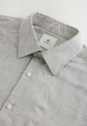 Camicia grigia chiaro con un sottile motivo floreale, colletto corto e bottoni bianchi. L'etichetta mostra il nome del marchio "NEXT". Texture del tessuto liscia.