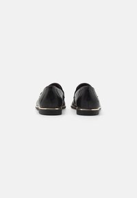 Scarpe in pelle nera con una superficie liscia, dotate di un accento metallico oro alla base e un design con punta rotonda.