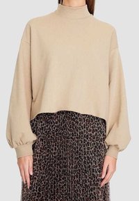 Sudadera recortada beige con un alto cuello y mangas abullonadas, combinada con una falda plisada de estampado animal en tonos marrón y negro.