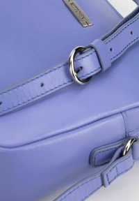 Borsa in pelle viola con una texture liscia, tracolla regolabile con hardware in argento e un accento metallico con marchio.