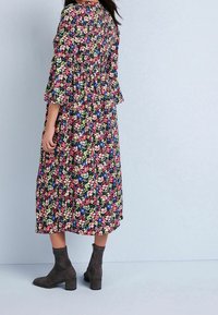 Vestido midi floral en tejido oscuro, con estampados vibrantes en rosa, púrpura y verde. Terminación con mangas acampanadas y cintura ajustada.