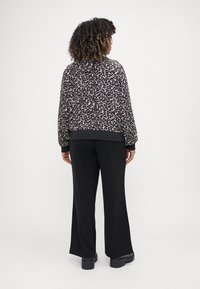 Jachetă bomber cu imprimeu de leopard, cu manșete și tiv elastic, asortată cu pantaloni largi negri și încălțăminte masivă neagră.