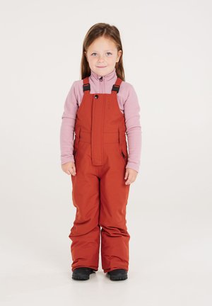 Rote wasserdichte Latzhose mit verstellbaren Trägern, kombiniert mit einem hellrosa Langarmshirt. Verfügt über Reißverschlusstaschen und eine lockere Passform.