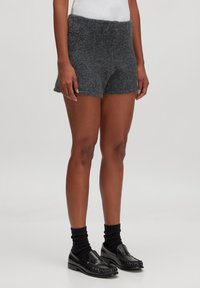Grijze gebreide shorts met een brede tailleband, een iets losse pasvorm en een zachte textuur. Gecombineerd met zwarte instappers en donkere sokken.