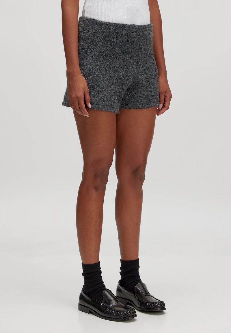 Grijze gebreide shorts met een brede tailleband, een iets losse pasvorm en een zachte textuur. Gecombineerd met zwarte instappers en donkere sokken.
