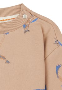Sweatshirt beige clair avec un col côtelé, illustré de poissons bleus et bruns, avec une fermeture à pression à l'épaule.