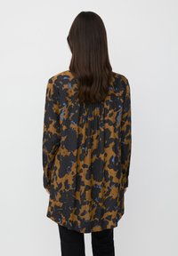 Camisa de manga larga con estampado de leopardo en tonos marrones y negros, con detalles en azul, de corte holgado y con un yugo recogido en la parte posterior. Textura ligera.