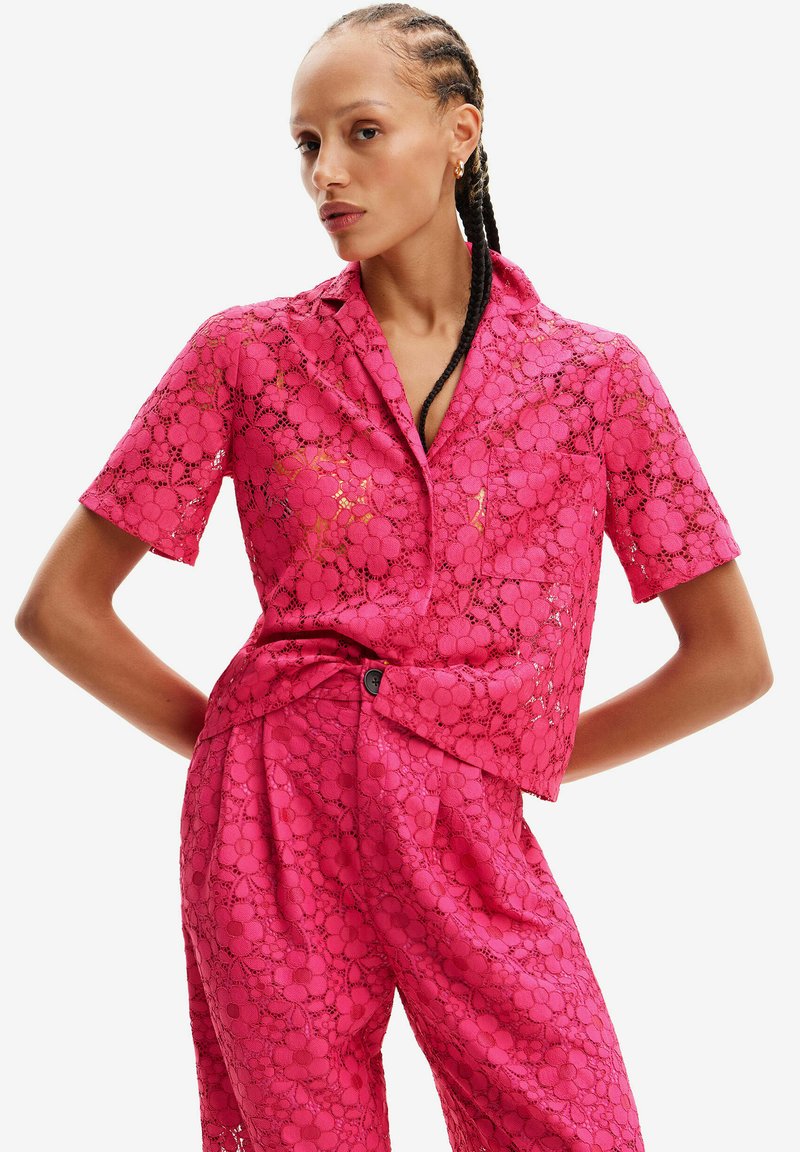 Lyserød blonder kortærmet skjorte med blomsterprint, knap-åben krave og en afslappet pasform. Matchet med bukser i samme materiale.